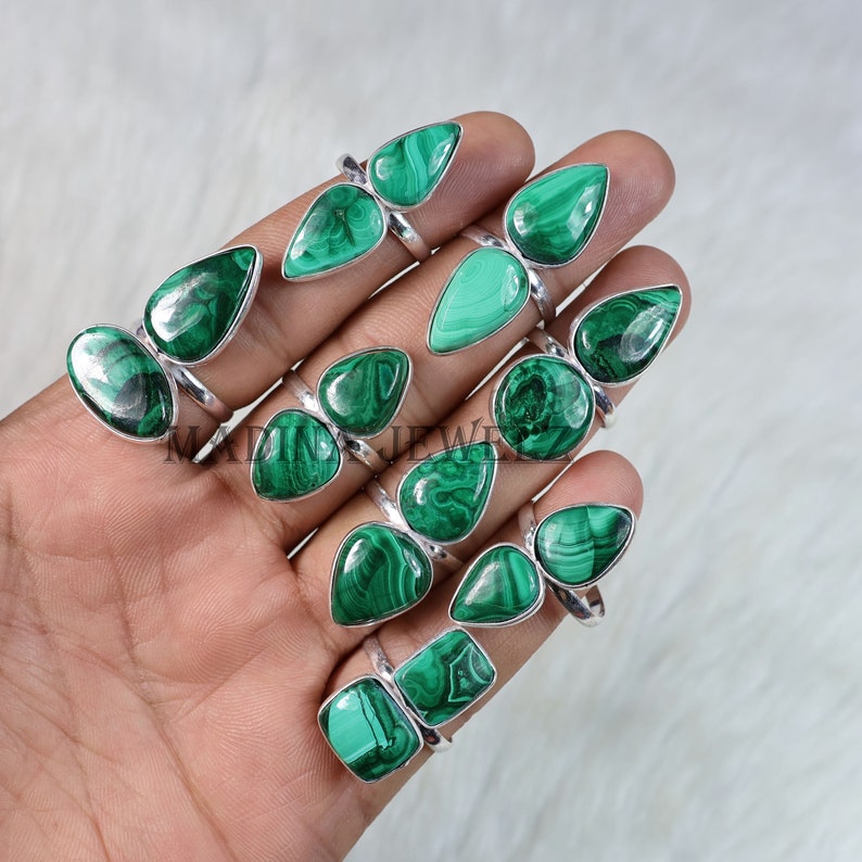 Pu&ograve; includere: Una collezione di 14 anelli d'argento con pietre preziose in malachite verde. Gli anelli presentano pietre a forma di goccia e sono esposti su una mano.