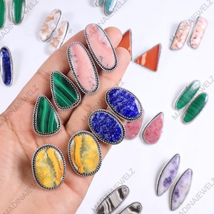 May include: A collection of gemstone rings in various shapes and colors, including green malachite, pink, blue lapis, and yellow. Each ring has a silver-colored, twisted rope-like border.