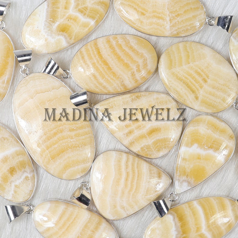 Pu&ograve; includere: Un assortimento di pendenti lucidi giallo chiaro con bails color argento. I pendenti hanno un motivo naturale a strisce e sono di varie forme, tra cui ovale e a goccia. Il testo "MADINA JEWELZ" &egrave; visibile.