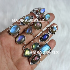 Puede incluir: Una colección de anillos de plata con piedras preciosas de labradorita iridiscente. Los anillos presentan varios diseños, incluyendo una forma de lágrima, ovalada y cuadrada. Las piedras tienen un brillo azul, verde y dorado.