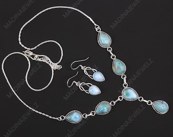 Könnte beinhalten: Ein silbernes Halsketten- und Ohrring-Set mit tropfenförmigen, hellblauen Edelsteinen. Die Halskette hat eine filigrane Kette, und die Ohrringe haben ein einzigartiges, offenes Design. Der Schmuck wird vor schwarzem Hintergrund präsentiert.