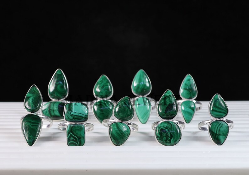 Pu&ograve; includere: Una collezione di dieci anelli d'argento con pietre preziose di malachite verde. Gli anelli presentano una variet&agrave; di forme, tra cui gocce e quadrati.