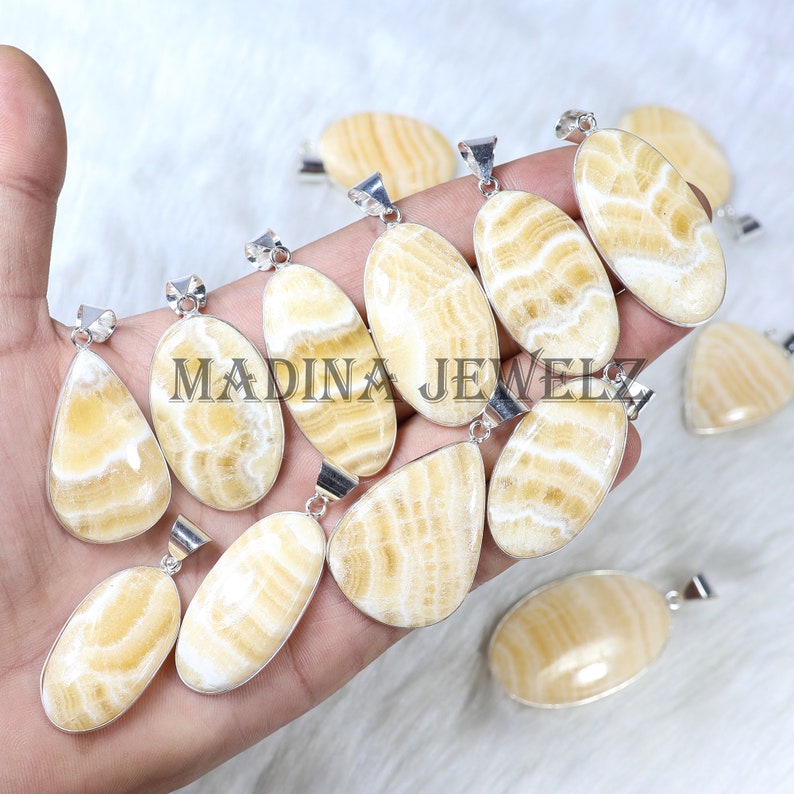 Pu&ograve; includere: Una collezione di collane con ciondoli con bails color argento. I ciondoli sono ovali e a goccia, con un motivo a righe crema e bianco. Il testo "MADINA JEWELZ" &egrave; visibile sui ciondoli.