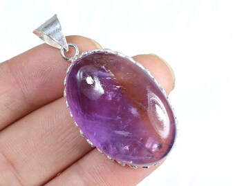 May include: Oval-shaped pendant with a polished, translucent purple and brown gemstone. The stone is set in a silver-colored metal frame with a decorative edge and a loop for a chain.