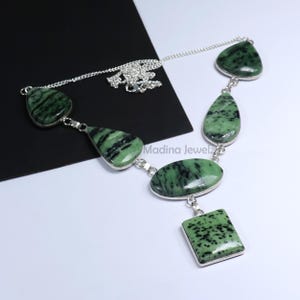 May include: A silver necklace featuring a series of green and black stone pendants in various shapes, including teardrops, ovals, and a square. The stones are set in silver bezels and connected by a delicate silver chain.