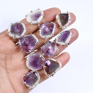 以下が含まれることがあります： アメジストの宝石をセットした銀の指輪10個のセット。指輪は、アメジストの形状とサイズが様々で、それぞれが独特の自然な外観をしています。アメジストは、白いインクルージョンが入った濃い紫色をしています。