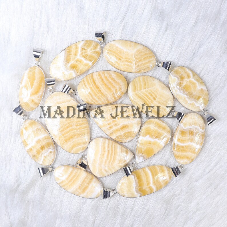 Pu&ograve; includere: Una collezione di pendenti ovali e di forma irregolare con anelli color argento. I pendenti sono di colore giallo chiaro con un motivo a righe. Il testo "MADINA JEWELZ" &egrave; stampato sui pendenti.