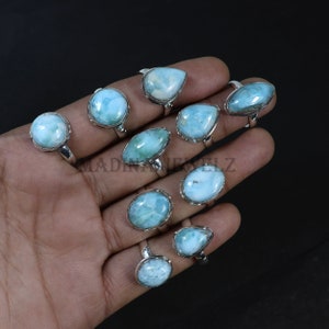 Pode incluir: Uma cole&ccedil;&atilde;o de an&eacute;is de prata esterlina com pedras preciosas de larimar azul claro em v&aacute;rias formas. Os an&eacute;is s&atilde;o exibidos em um fundo escuro, mostrando as pedras polidas e as configura&ccedil;&otilde;es de prata. As pedras preciosas t&ecirc;m uma apar&ecirc;ncia marmorizada.