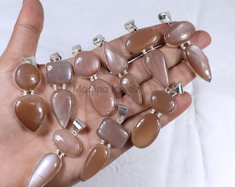 Puede incluir: Una colección de 12 colgantes de piedra de sol plateados, con una variedad de formas y tamaños. Los colgantes se muestran en una mano, mostrando su brillo y color únicos.