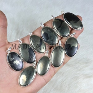 May include: A selection of oval pyrite pendants with silver frames. The pyrite stones display a metallic sheen, with colours ranging from gold to dark grey. Each pendant features a small loop at the top for a chain, ready to wear.