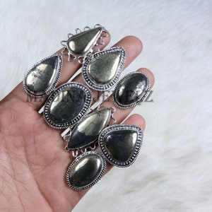 Puede incluir: Una colección de siete colgantes plateados con piedras de pirita. Las piedras son de color gris oscuro con un brillo metálico. Los engastes son de diferentes formas, incluyendo gota, ovalada y redonda.