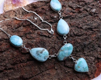 Könnte beinhalten: Eine silberne Halskette mit ovalen und tropfenförmigen blau-grünen Larimar-Edelsteinen. Die Halskette wird auf einer strukturierten, dunkelbraunen Holzoberfläche präsentiert. Der Text "Madina jewlz" ist auf der Halskette zu sehen.