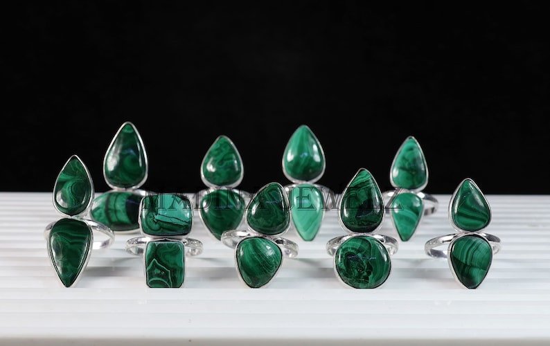 Pu&ograve; includere: Una collezione di nove anelli d'argento con pietre preziose di malachite verde. Gli anelli presentano una variet&agrave; di forme e dimensioni di malachite, tra cui forme a goccia e quadrate.
