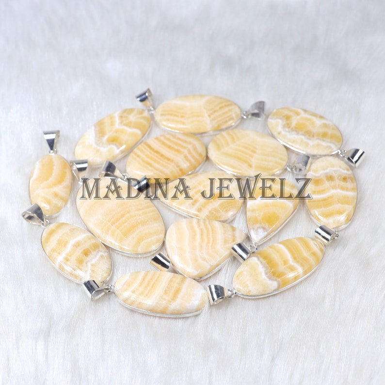 Pu&ograve; includere: Una collezione di pendenti ovali e a goccia con anelli color argento. I pendenti presentano un motivo a righe giallo chiaro e crema. Il testo "MADINA JEWELZ" &egrave; visibile nell'immagine.