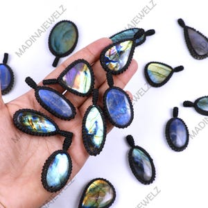 Peut inclure: Un ensemble de 11 pendentifs en labradorite avec un cordon en macramé noir. Les pendentifs sont de formes et de tailles variées, notamment en forme de larme, ovale et ronde. Les pierres de labradorite sont irisées et présentent une gamme de couleurs, notamment le bleu, le vert et l'or.