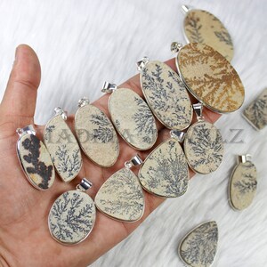 May include: A collection of 11 dendritic agate pendants with silver bail settings. The pendants are oval and teardrop shaped and feature a variety of brown and black dendritic patterns.