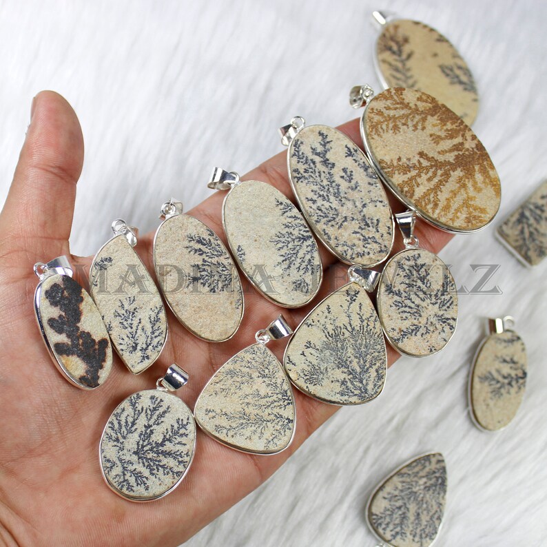 May include: A collection of 11 dendritic agate pendants with silver bail settings. The pendants are oval and teardrop shaped and feature a variety of brown and black dendritic patterns.