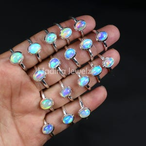 Könnte beinhalten: Eine Sammlung von Silberringen, jeder mit einem ovalen Opal-Edelstein. Die Opale zeigen eine Farbpalette, darunter Blau, Grün und Gelb. Die Ringe werden auf einer Hand vor dunklem Hintergrund präsentiert.