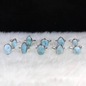 Pode incluir: Uma cole&ccedil;&atilde;o de an&eacute;is de prata com pedras de larimar ovais, em forma de gota e redondas. As pedras, em tons de azul claro e branco, s&atilde;o engastadas em bandas de prata polida. Exibidos sobre uma superf&iacute;cie branca e texturizada.