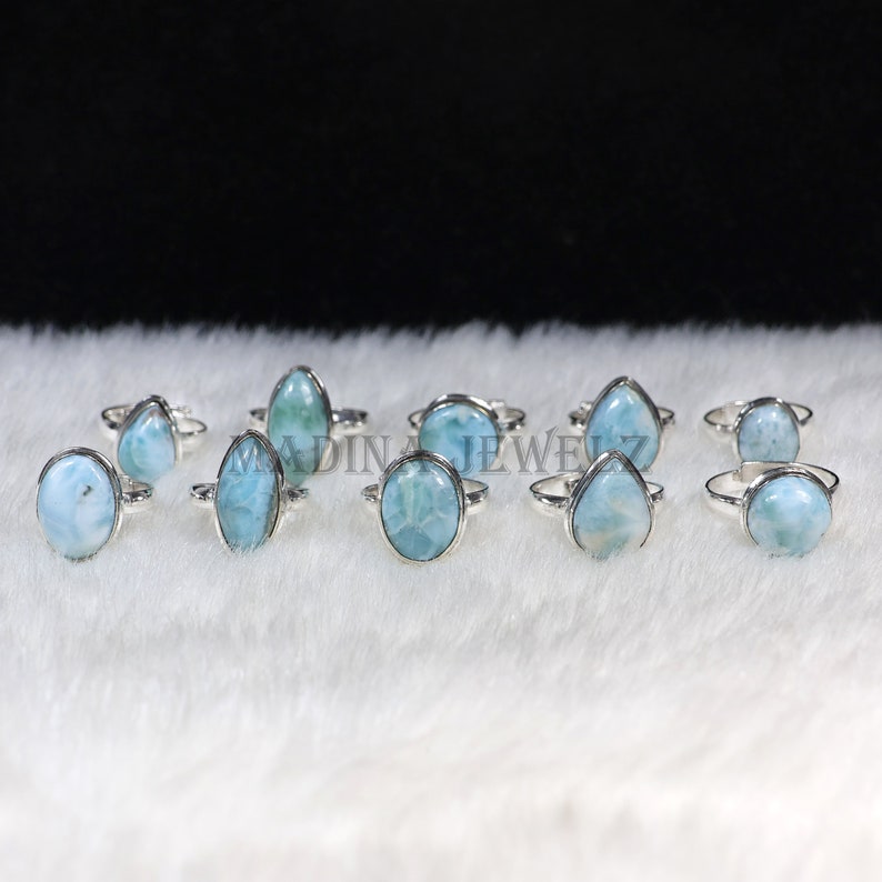 Pode incluir: Uma cole&ccedil;&atilde;o de an&eacute;is de prata com pedras de larimar ovais, em forma de gota e redondas. As pedras, em tons de azul claro e branco, s&atilde;o engastadas em bandas de prata polida. Exibidos sobre uma superf&iacute;cie branca e texturizada.