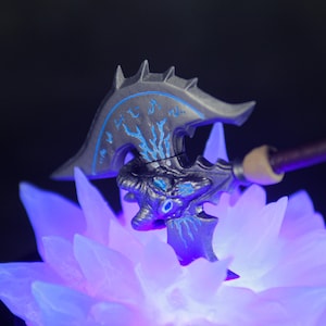 May include: A black and blue axe with a detailed design, resting on a purple and blue crystal base. The axe has a sharp blade and a handle with a skull-like design.