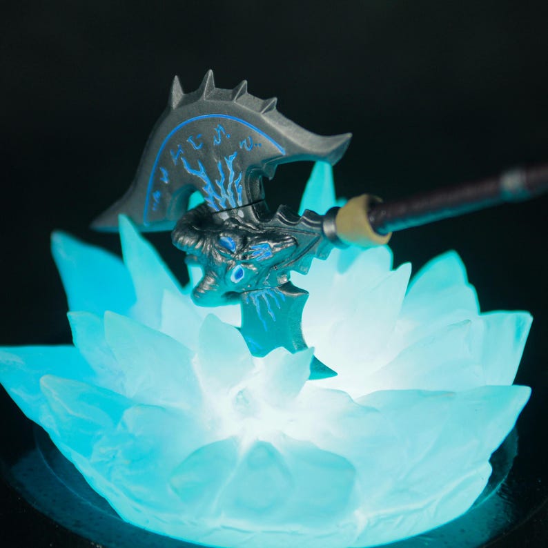 May include: A black and blue axe with a glowing blue base. The axe has a skull-like design and is surrounded by a blue crystal-like base.