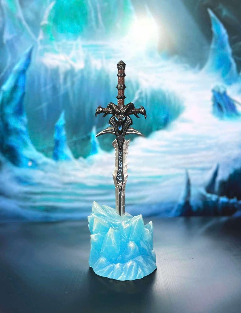 May include: A silver and black sword with a skull-like handle, standing upright on a blue ice-like base. The sword has intricate details and runes along the blade.