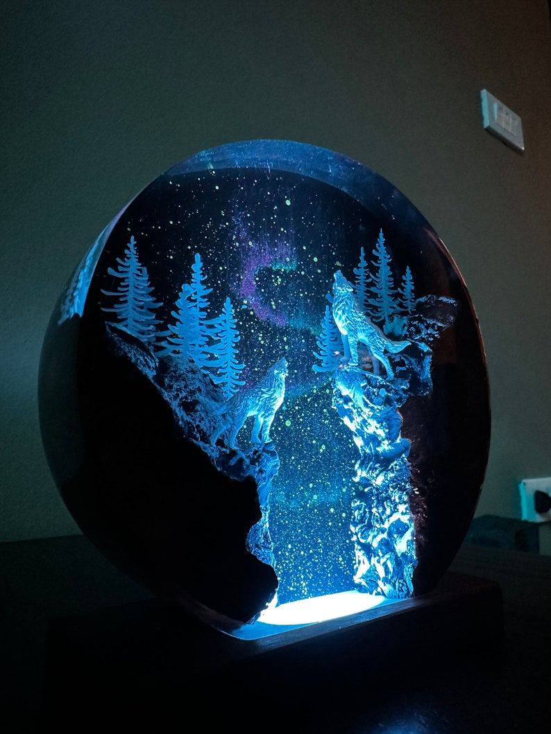 May include: A glass dome with a glowing blue light inside. The dome contains a scene of two wolves howling at the moon, surrounded by trees and a starry sky.