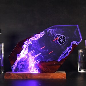 May include: A resin and wood sculpture of a Star Wars X-Wing fighter and a TIE fighter in a purple and red light. The sculpture is on a wooden base.