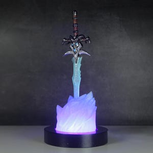 May include: A blue and purple light-up display featuring a silver sword with a black handle and a skull-like design. The sword is on a base that looks like a frozen flame.