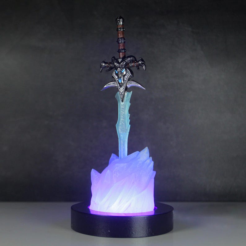 May include: A blue and purple light-up display featuring a silver sword with a black handle and a skull-like design. The sword is on a base that looks like a frozen flame.
