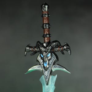 May include: A black and silver sword with a skull-like design and blue glowing eyes. The sword has a brown leather handle with metal accents.