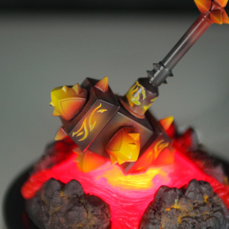 May include: A fiery, spiked hammer figurine with a glowing red base. The hammer is made of dark brown and orange plastic with yellow accents. The base is made of black plastic and has a red glow.