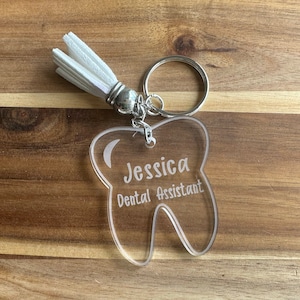 May include: A clear acrylic tooth-shaped keychain with a white tassel. The keychain is engraved with the name "Jessica" and the words "Dental Assistant".