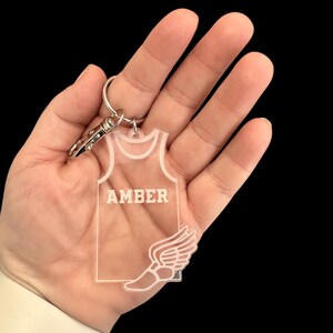 May include: A clear acrylic keychain shaped like a running jersey with the name "AMBER" printed on the front and a winged running shoe on the bottom.