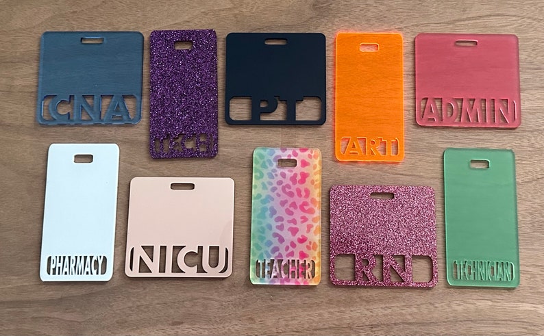 May include: Ten different name tags with various colours and patterns. The name tags are made of clear acrylic with the text cut out. The text on the name tags includes "CNA", "L&D", "PT", "ART", "ADMIN", "PHARMACY", "NICU", "TEACHER", "RN", and "TECHNICIAN".