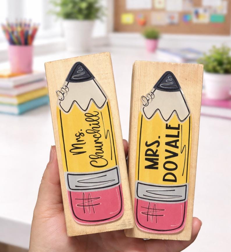 May include: Two wooden stamps with pencil designs. The pencils are yellow with pink erasers and gray tips. One stamp reads "Mrs. Churchill" and the other reads "Mrs. Dovale".