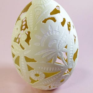 May include: A white egg with intricate floral carvings, creating a delicate lace-like pattern. The egg is illuminated from behind, highlighting the intricate details of the carving.