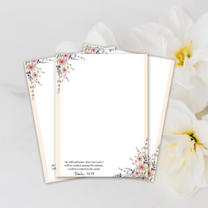May include: Three sheets of stationery with floral corner designs in pink, purple, and green. The text "Be still and know that I am God" is printed on the bottom right corner. The stationery has a light peach border.