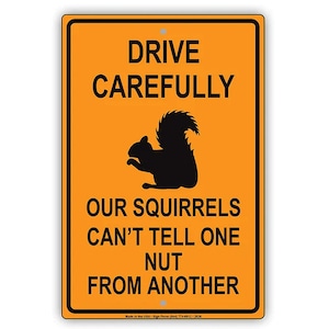May include: Orange metal sign with black text and a silhouette of a squirrel. The sign reads "Drive Carefully Our Squirrels Can't Tell One Nut From Another."