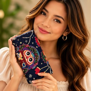May include: A rectangular navy blue wallet featuring a vibrant, multi-colored embroidered owl design with large circular eyes, surrounded by small white star-like patterns and floral accents on a dark fabric background.
