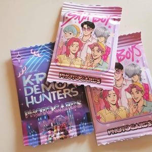May include: Three packs of photocards featuring anime-style illustrations of young men. The packs are in shades of purple and pink, with the words "Boys", "K-P Demo Hunters", and "Photocards" visible.