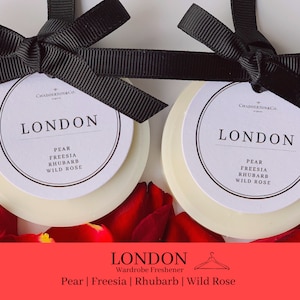 Könnte beinhalten: Zwei weiße runde Kleiderschrank-Dufttabletten mit schwarzen Schleifen. Die Dufttabletten haben ein weißes Etikett mit dem Text "CHADDERTON&CO. LONDON" und der Duftbeschreibung "PEAR FREESIA RHUBARB WILD ROSE".
