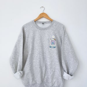 May include: A gray sweatshirt with a small embroidered graphic of a blue bird in a computer screen with the text "PSG" on the front.