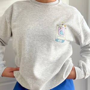 May include: A heather grey sweatshirt with a cartoon goose wearing a blue shirt and a badge that says "Registered Sad Goose" and "RSG".