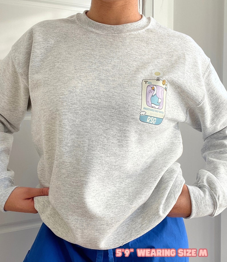 May include: A heather grey sweatshirt with a cartoon goose wearing a blue shirt and a badge that says "Registered Sad Goose" and "RSG".