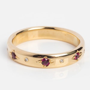 Puede incluir: Un anillo de banda de oro con engastes en forma de estrella, cada uno con una piedra preciosa roja y pequeños diamantes. El anillo tiene un acabado pulido y un diseño clásico, adecuado para el uso diario o ocasiones especiales.