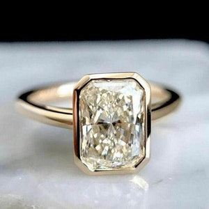 May include: A gold engagement ring with a large, clear, rectangular-shaped diamond set in a bezel setting.
