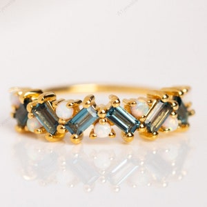 May include: A gold band ring with a row of alternating blue and white gemstones. The blue gemstones are rectangular and the white gemstones are round.