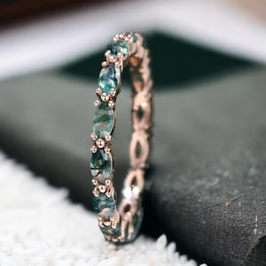 Può includere: Una fascia di eternità in oro rosa con una fila di pietre preziose verdi. L'anello è incastonato con pietre di forma ovale.